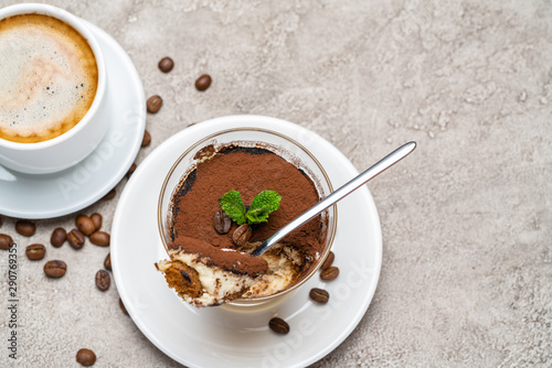 Portion of Classic tiramisu dessert in a glass and cup of coffee on concrete background