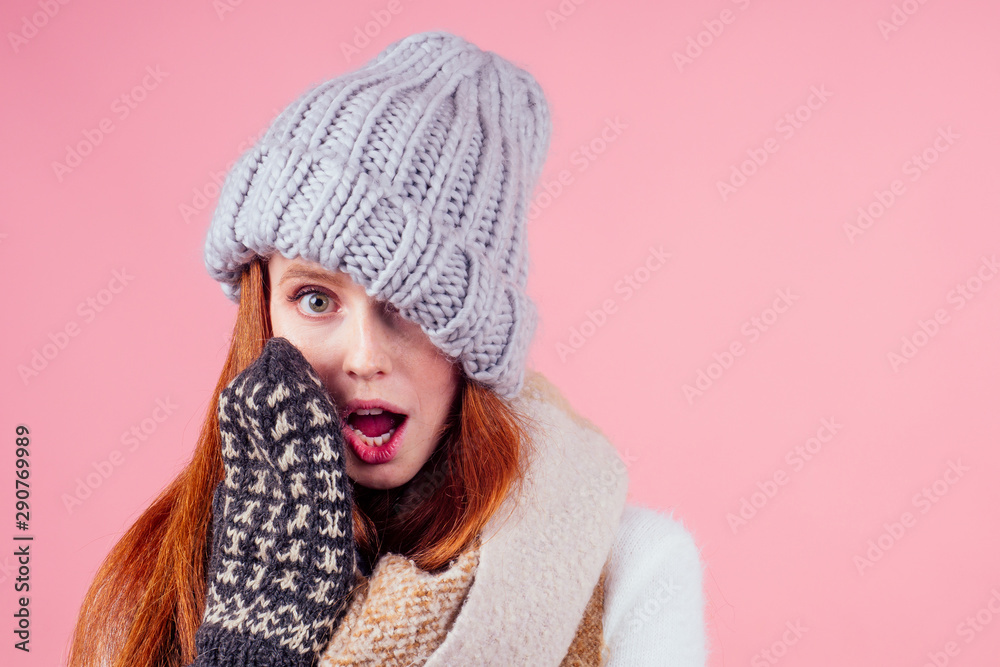 amazed and surprised redhaired ginger woman wearing stylish hat ,knitted mittens and sweater gossiping in studio pink background