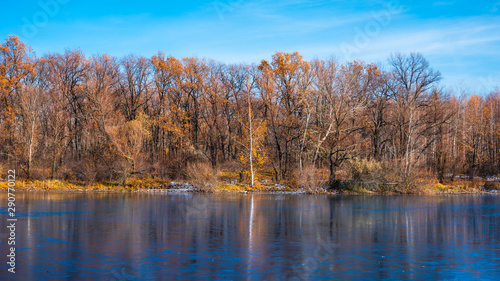 Beautiful forest landscape at the beginning of winter - forest lake with first ice and trees on the shore