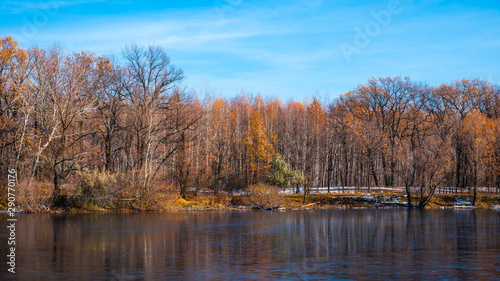 Beautiful forest landscape at the beginning of winter - forest lake with first ice and trees on the shore