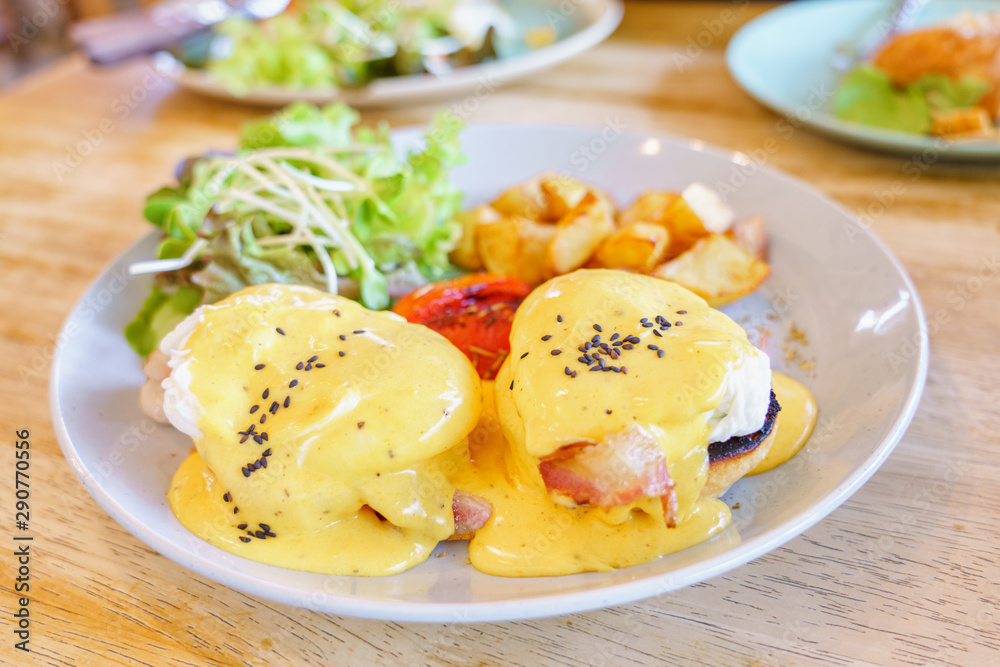 Close up egg benedict with organic salad and fried potato on with dish on wooden table background. delicious breakfast in morning..