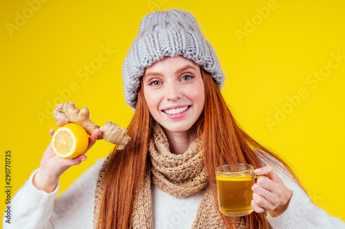 sick illness redhaired woman good looking wearing knitted sweater and hat with scarf drinking hot tea cup with lemon and ginger in studio yellow background
