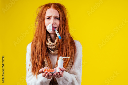 unwell redhaired ginger woman runny nose wearing knitted sweater and scarf with many pills in hand in studio yellow background photo