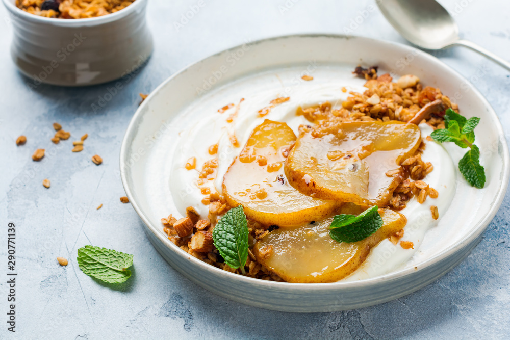 Greek yogurt with caramelized pear, granola, nuts and melted sugar for a wholesome breakfast on a gray ceramic plate. Rustic style. Top view. Greek yogurt with caramelized pear, granola, nuts and melted sugar for a wholesome breakfast on a gray ceramic plate. Rustic style. Top view.