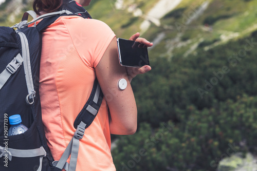 Active life of diabetics, woman hiking and checking glucose level with a remote sensor and mobile phone, sensor checkup glucose levels without blood photo