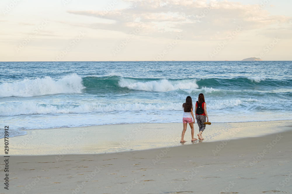 Madre e hija caminado en la playa en el atardecer
