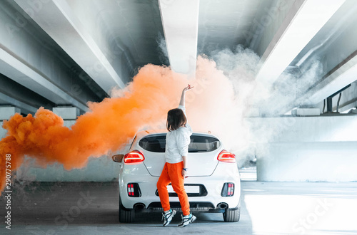 Confident and beautiful young woman in casual sports wear dancing near new car and rejoycing.