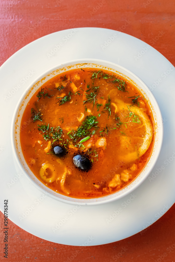 Russian red soup Solyanka, with sausage, olives and lemon. top view on the red table. close up vertical