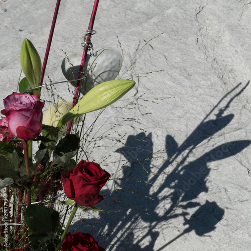 In the front details of a bunch of flowers and shadows of the bouquet on a stone in the background.