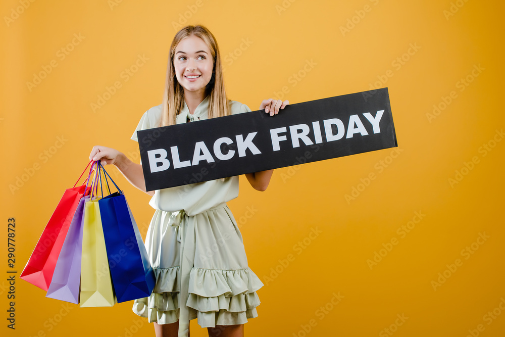 happy smiling pretty girl has black friday sign with colorful shopping bags isolated over yellow happy smiling pretty girl has black friday sign with colorful shopping bags isolated over yellow
