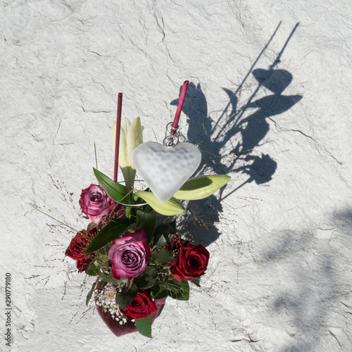 Beautiful arranged floral bouquet with Red Naomi and Deep Purple roses on a stony background. Purple sleeve around the flowers at the bottom and on the top of the bouquet a white heart as decoration.