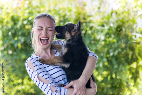 Happy girl holding a German shepherd puppy and smiling. Buying and acquiring a dog, the joy of meeting. The dog bites and kisses the owner. On a blurred green background. copy space