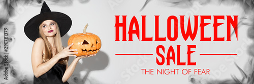 Young blonde woman in black hat on scary white background. Attractive caucasian female model smiling. Halloween sales, black friday, cyber monday, autumn concept. Flyer for your ad. Holding pumpkin.