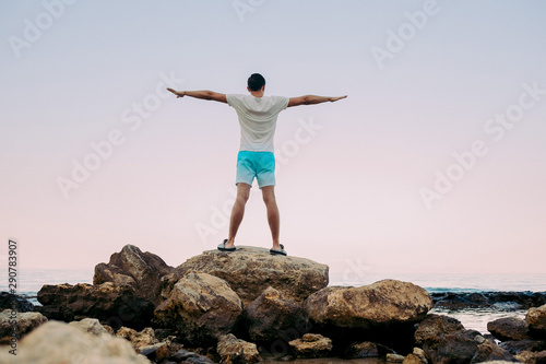 Young man standing with raised hands on top of a mountain sea and enjoying view. man enjoying the sensation of freedom in front of setting sun
