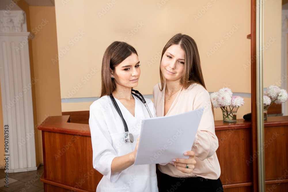 Young female doctor meets with the client at reception. The doctor tells the patient about the types of services and records the girl for an appointment Young female doctor meets with the client at reception. The doctor tells the patient about the types of services and records the girl for an appointment