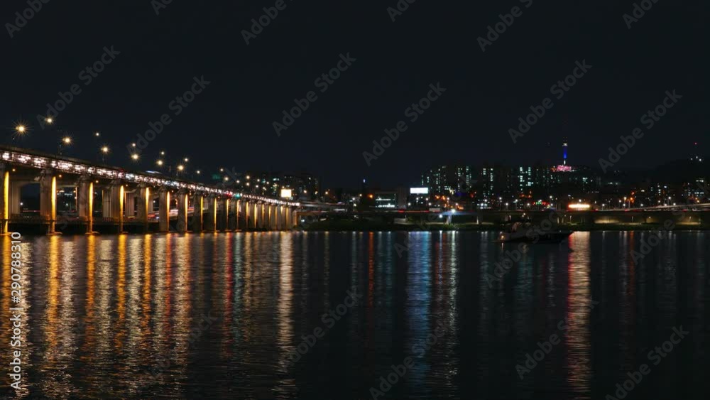 Zoom out night time lapse on the Han River, Seoul South Korea, the iconic Banpo bridge and Namsan Tower. The foreground features a tourist boat and reflections of city lights on the water Zoom out night time lapse on the Han River, Seoul South Korea, the iconic Banpo bridge and Namsan Tower. The foreground features a tourist boat and reflections of city lights on the water