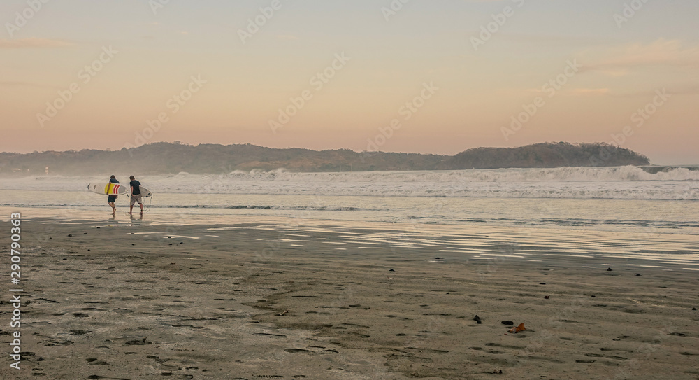 Naklejka premium Surfers at sunset on the beach