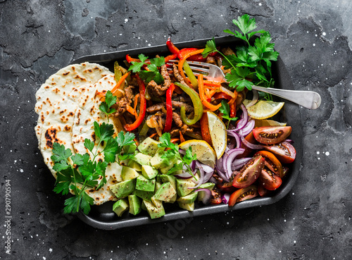 Spicy beef, vegetables, avocado, corn tortillas fajitas on a sheet pan on a dark background, top view. Delicious snack, tapas in mexican style