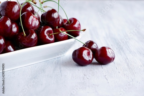 Fresh juicy sweet dark red sweet cherry in a white ceramic bowl on a light wooden background. The concept of a healthy breakfast, a snack. Closeup with selective focus.
