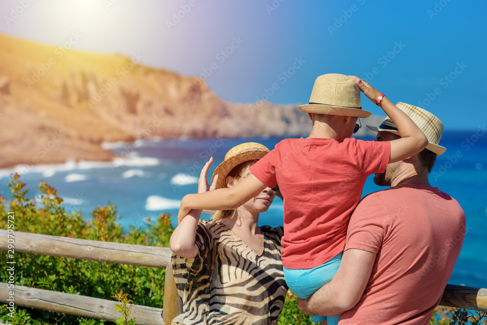 Family holidays. Mom, dad and son in sun hats standing on natural balcony against amazing sea view, they are longing this trip.