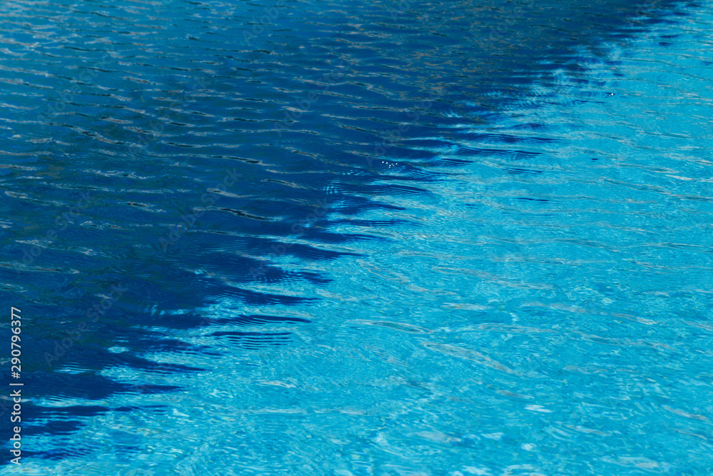 A two colored light and dark blue water with ripples and sunny reflections in a swimming pool.