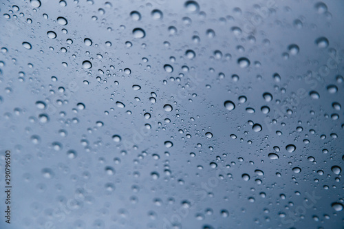 Close up of rain drops on the windshield, front window of a car on a blue gray background of dark sky.