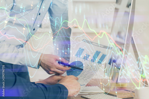 Double exposure of chart with businessman typing on computer in office on background. Concept of hard work.