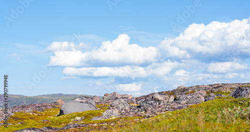 Huge rounded stones on backdrop of hills, small mountains and low Northern the sky. Over stones, hills and grass smoothly move huge white clouds