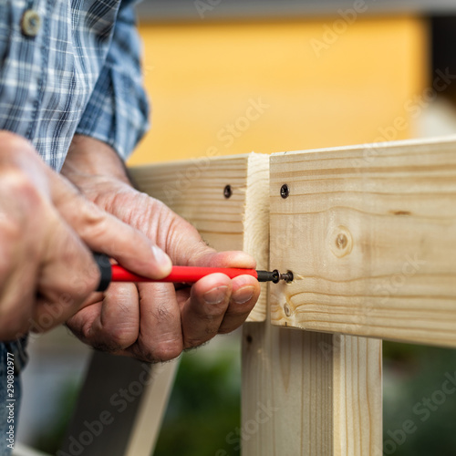 Adult carpenter craftsman with screwdriver screw the screw to fix the boards of a wooden fence. Housework do it yourself. Stock photography.