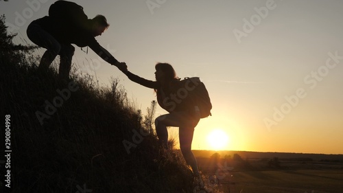 A male traveler holds out his hand to a female traveler climbing a hilltop. Tourists climb the mountain in the sunset  holding hands. teamwork of business people. Happy family on vacation.
