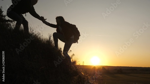 A male traveler holds out his hand to a female traveler climbing a hilltop. Tourists climb the mountain in the sunset, holding hands. teamwork of business people. Happy family on vacation.