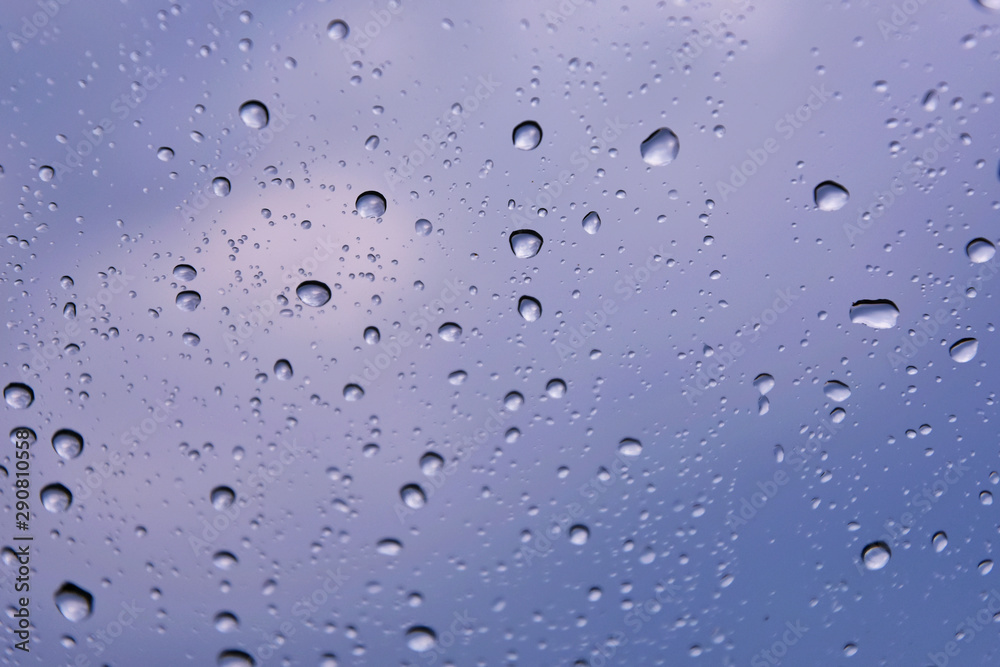 Rain drops with selective focus on transparent glass. Glass surface with water drops, violet toned. Window with raindrops. water drops on glass Rain drops with selective focus on transparent glass. Glass surface with water drops, violet toned. Window with raindrops. water drops on glass