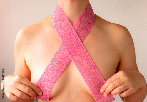 naked girl covers her breast with a pink ribbon - a symbol of breast cancer awareness day, close up, creative