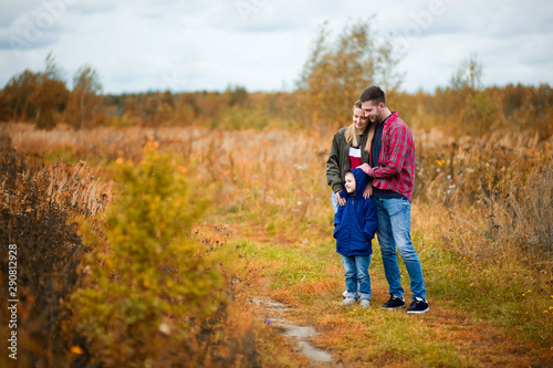 A young family - mom, dad and little son are standing on a country road in the fall afternoon. Parents smile warmly and look at their son © Вячеслав Думчев
