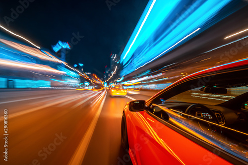 View from Side of a Red Muscle Car moving in a night city, Blured road with lights with car on high speed. Concept rapid rhythm of a modern city.