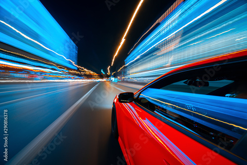 View from Side of a Red Muscle Car moving in a night city, Blured road with lights with car on high speed. Concept rapid rhythm of a modern city.
