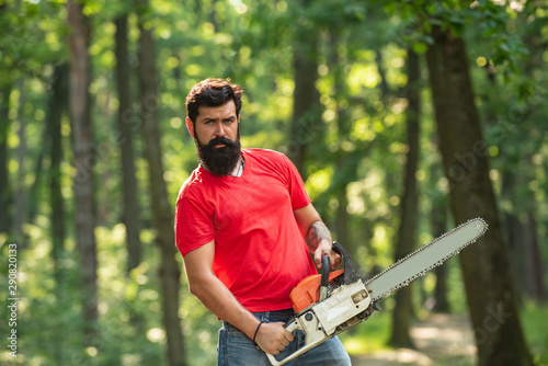 A handsome young man with a beard carries a tree. Illegal logging continues today. Lumberjack in the woods with chainsaw axe. photo