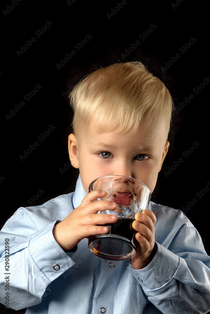 The boy is drinking juice from a glass cup. The boy is drinking juice from a glass cup.