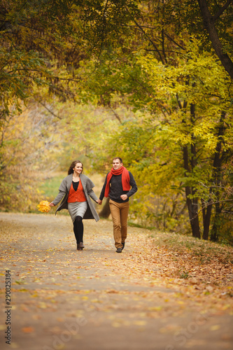 Couple weared in autumn-style clothes (oranfe scarf and vest) running through the autumn landscape. Alley covered with yellow foliage. Autumn walk outdoors. Two lovers in autumn park. Romantic dating © Olga Mishyna