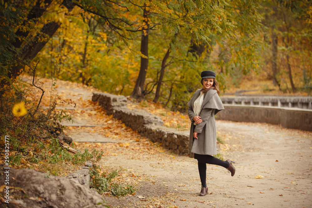 Fototapeta premium Autumn mood. Romantic woman weared in beige cloak walk in a park on background of beautifull autumn leaves. Smile. fall coming. Brown-haired girl with long hairs.