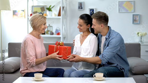 Adult children giving gift box to mother-in-law, celebrating birthday, attention