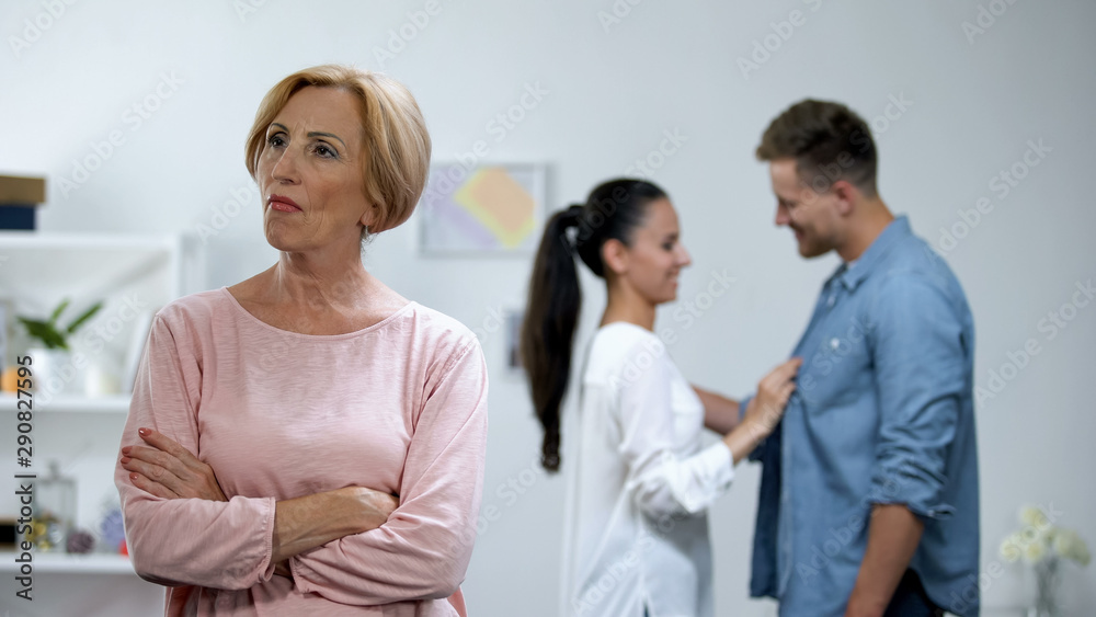 Angry mother with hands crossed, couple in love on background, lack of attention Angry mother with hands crossed, couple in love on background, lack of attention
