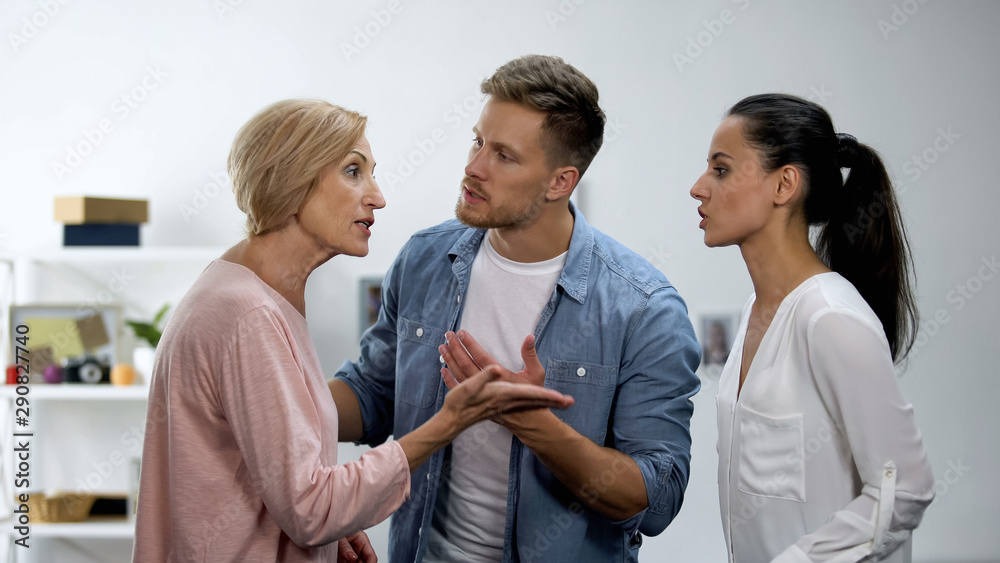 Fototapeta premium Young man settling conflict between mother and wife, family problems, quarrel
