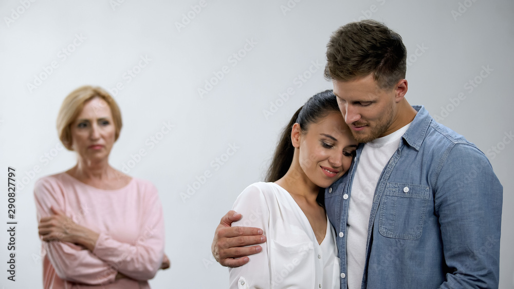 Offended mother-in-law looking at couple tenderly hugging, lack of attention Offended mother-in-law looking at couple tenderly hugging, lack of attention