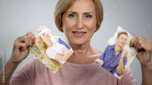 Tricky mother holding two parts of torn photo, happy to tear apart son family photo