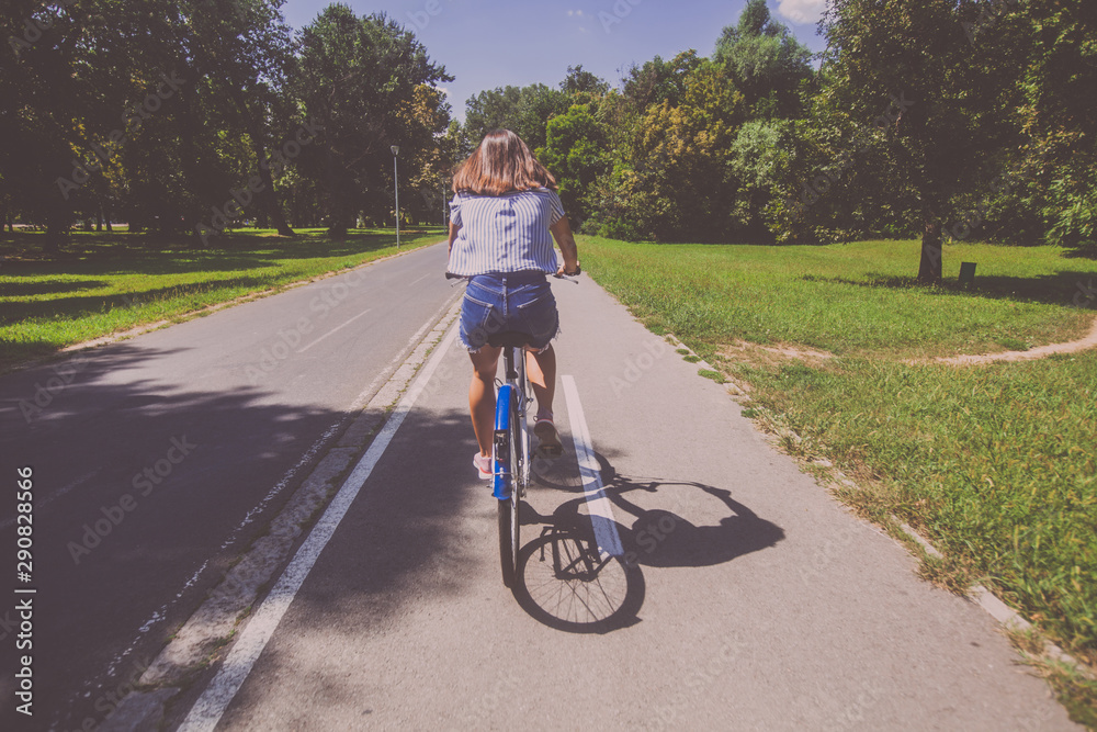 Obraz premium Pretty Young Woman Riding Bicycle In The Park Rear View