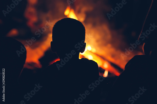 Boy sitting near campfire and looking at the flame.
