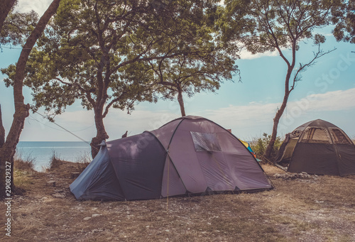 Large spacious tents on the coast. Two huge gray tents formed a camp on the seashore with all their equipment. Campfire, sunbeds, beach umbrella.