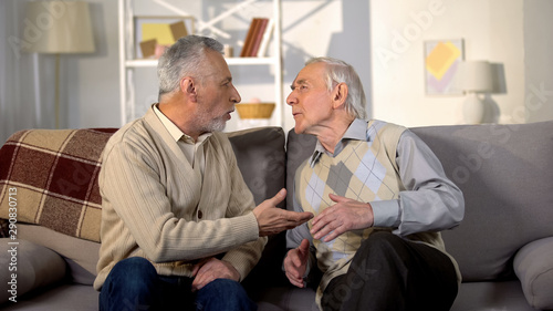 Aged male friends arguing on sofa at home, misunderstanding conflict, quarrel
