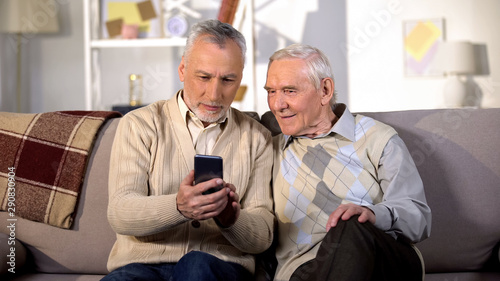 Glad senior friends watching online video by smartphone application, gadget